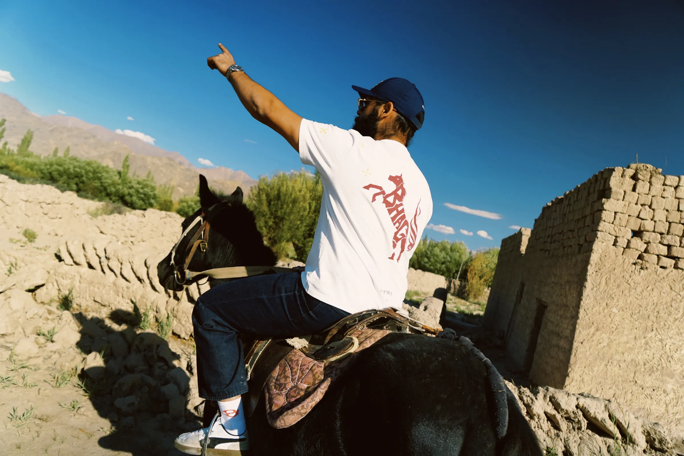 A rider on horseback pointing at the sky in a white tee with the rearing-horse back print