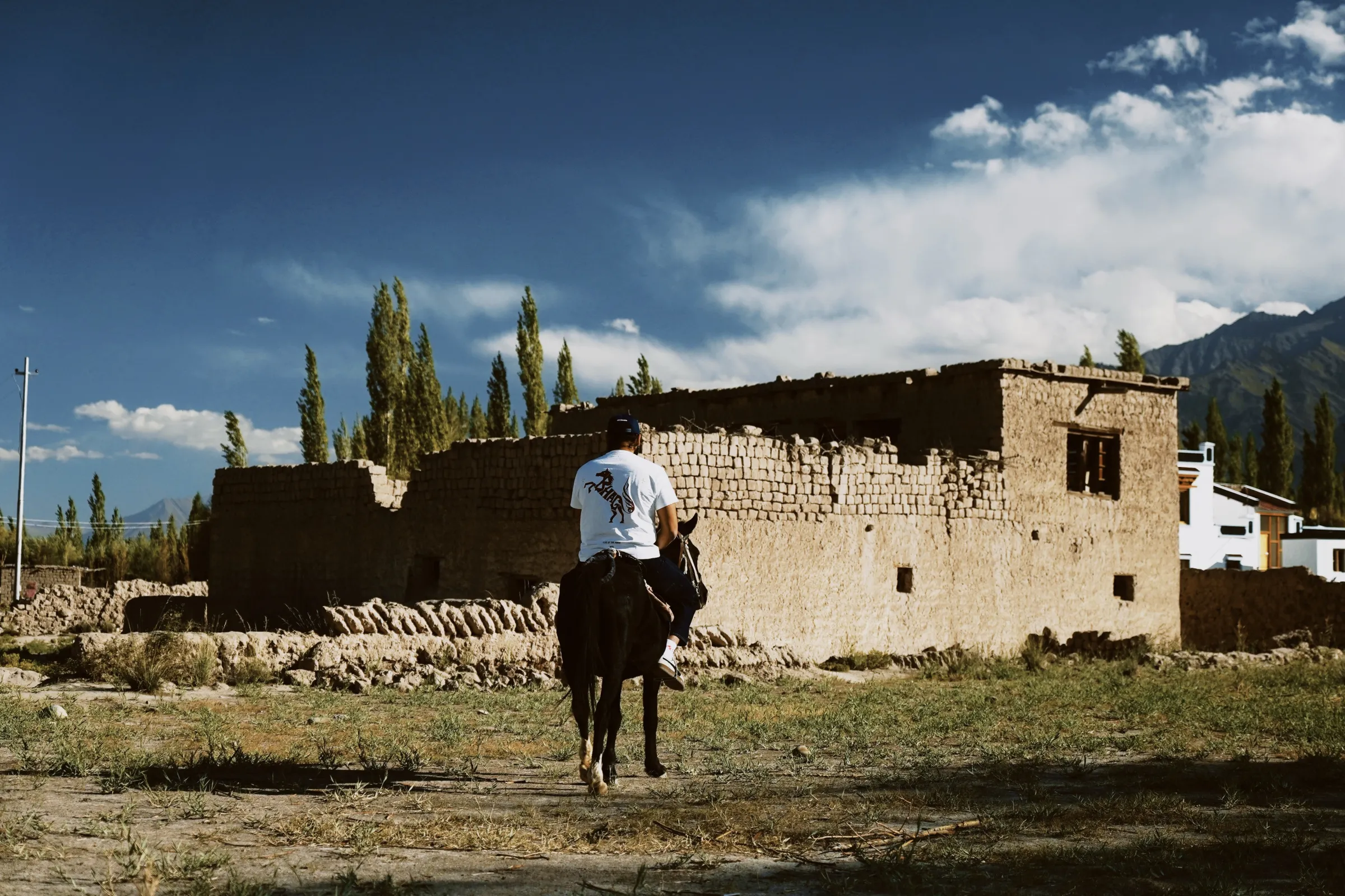 A rider in a white tee crossing a mud-brick village on horseback
