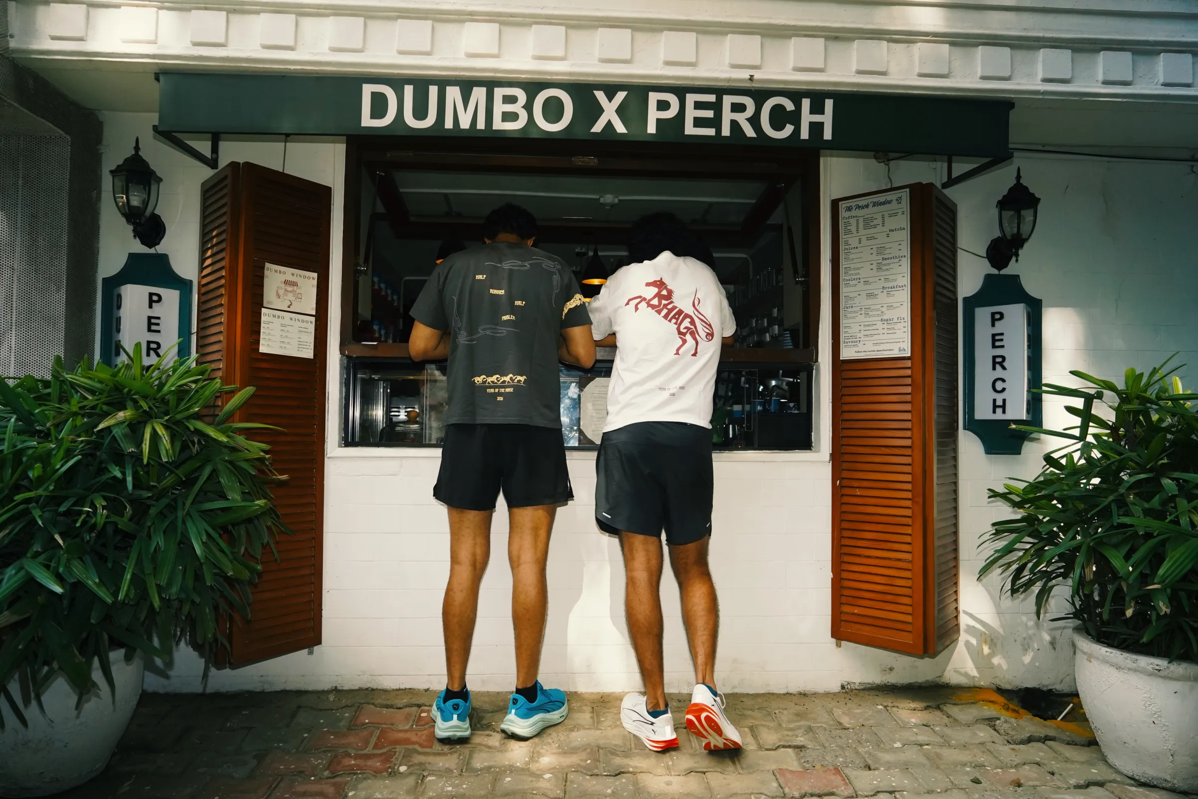 Two friends at a street-side window, one in the white rearing-horse tee