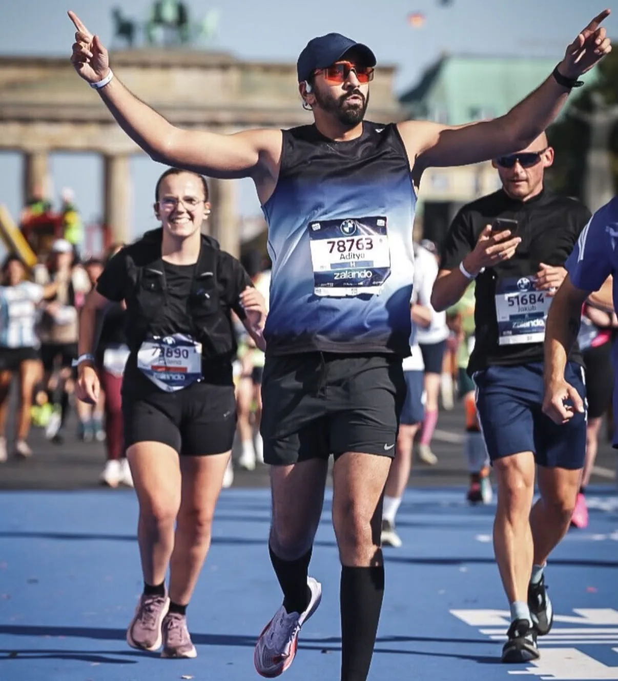 A runner in the Dark Aura Vest, arms raised at the Berlin Marathon finish by the Brandenburg Gate